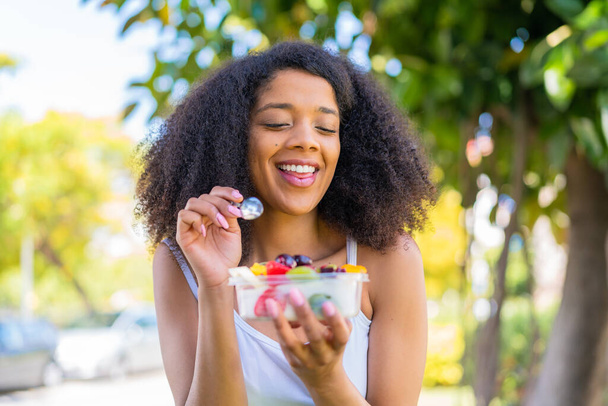 Genç Afrikalı Amerikalı bir kadın açık havada bir kase meyve tutuyor. - Fotoğraf, Görsel