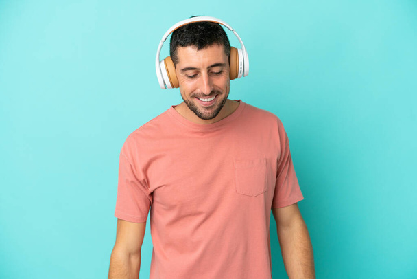 Νέος όμορφος καυκάσιος άνδρας απομονωμένος σε μπλε φόντο ακούγοντας μουσική - Φωτογραφία, εικόνα