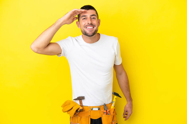 young electrician caucasian man isolated on yellow background looking far away with hand to look something - Photo, Image