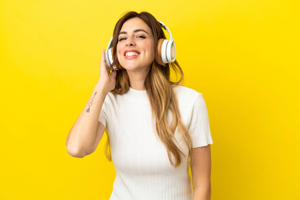 Caucasian woman isolated on yellow background listening music - 写真・画像