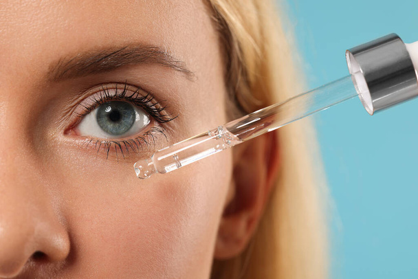 Woman applying cosmetic serum onto her face on light blue background, closeup - Foto, Bild