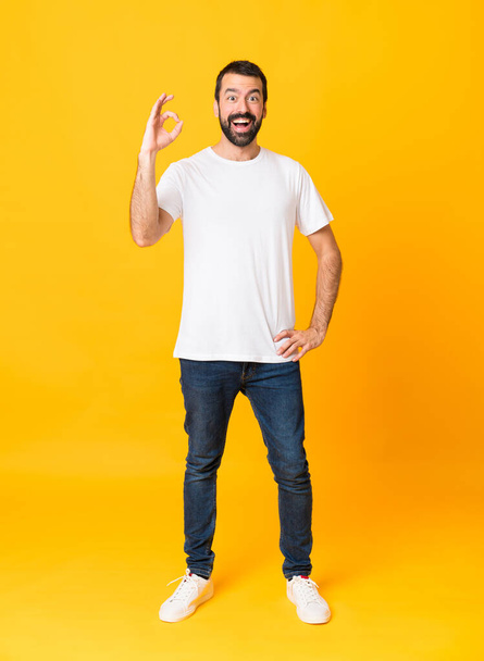 Full-length shot of man with beard over isolated yellow background surprised and showing ok sign - Photo, Image