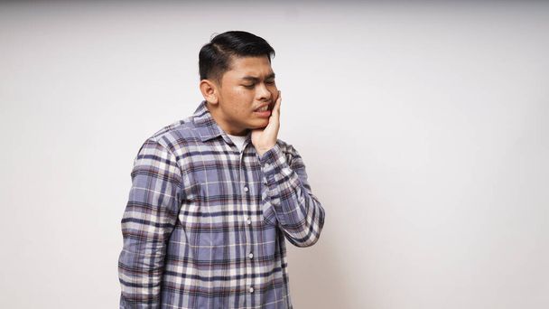 Diş ağrısı konsepti. Asyalı bir adam beyaz arka planda acı ifadesiyle çenesine dokunuyor. Stüdyo çekimi - Fotoğraf, Görsel