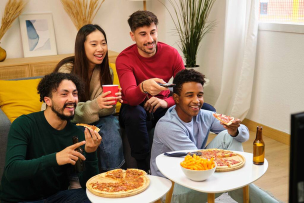 Ομάδα φίλων τρώει πίτσα και βλέποντας μια ταινία σε μια κοινόχρηστη φοιτητική εστία. - Φωτογραφία, εικόνα