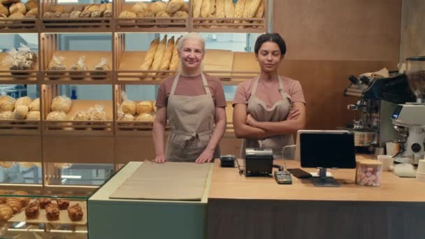 Inzoomen portretfoto van multi-etnische oudere en jonge vrouwelijke werknemers die bij de kassa in de bakkerij staan en met een glimlach voor de camera poseren - Video