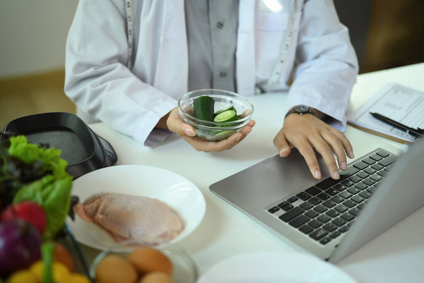 Професійний дієтолог використовує ноутбук і готує план харчування для пацієнта в клініці - Фото, зображення