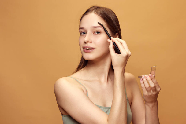 Young pretty woman holds make up palette, looking at camera and doing nude make up against beige background. Concept of natural beauty and make up, fashion, style. Copy space for ad. - Photo, image