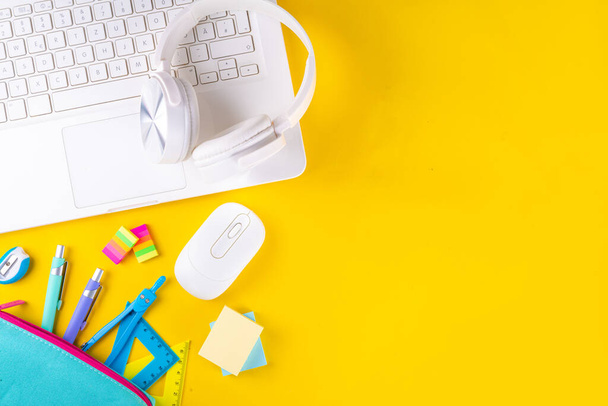 Zurück zur Schule, Online-Bildung hohen farbigen leuchtend gelben Hintergrund. Weißer Laptop mit Schulmaterial, Kopfhörer, Mäppchen und Zubehör von oben - Foto, Bild