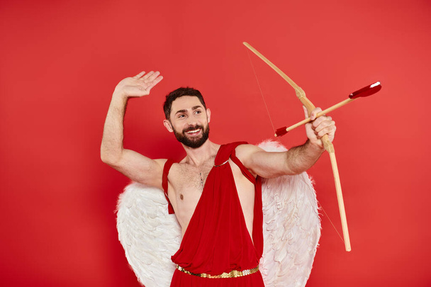 homme gai en costume de Cupidon tir à l'arc avec flèche en forme de coeur sur rouge, st fête costume de Saint-Valentin - Photo, image