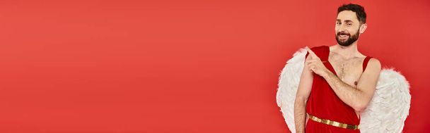 drôle homme cupide barbu regardant la caméra et pointant du doigt sur rouge, bannière horizontale - Photo, image