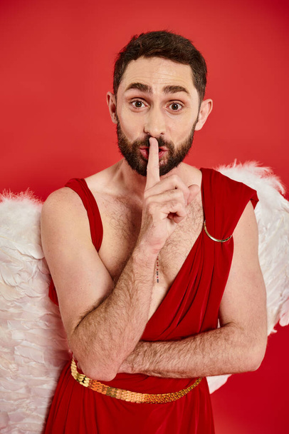 αστείο γενειοφόρος άνδρας ντυμένος ως cupid δείχνει Hush σημάδι και κοιτάζοντας κάμερα στο κόκκινο, Άγιος Βαλεντίνος ημέρα - Φωτογραφία, εικόνα