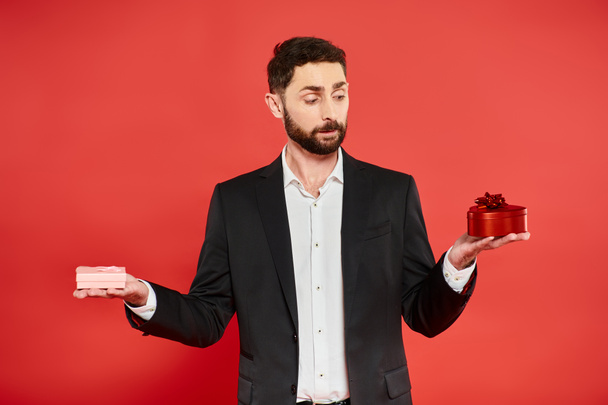 elegáns szakállas üzletember fekete öltönyben választott Szent Valentin nap jelen piros háttér - Fotó, kép