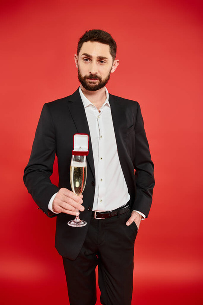 uomo in completo nero con bicchiere di champagne e confezione regalo con anello gioiello rosso, San Valentino - Foto, immagini