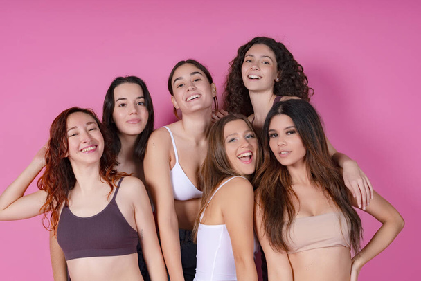 Gruppe von sechs unterschiedlichen Frauen lächelt und umarmt und strahlt körperliche Positivität vor einem verspielten rosa Hintergrund aus. - Foto, Bild