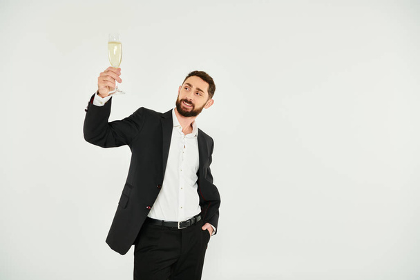 glücklicher erfolgreicher Geschäftsmann im schwarzen Anzug, der am Valentinstag auf grau mit Champagner anstößt - Foto, Bild