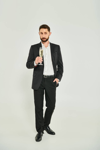 knappe zakenman in zwart pak met champagne en hand in hand op grijs, st valentines concept - Foto, afbeelding