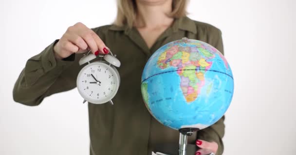 Una mujer sostiene un globo y un despertador, un primer plano. Concepto, hora mundial, meridiano de Greenwich - Imágenes, Vídeo