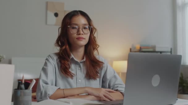 Portrait de femme asiatique assise au bureau devant un ordinateur sans fil et travaillant de la maison, regardant la caméra - Séquence, vidéo