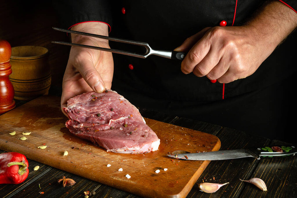 Preparing a steak from meat by the hands of a chef for a barbecue. Raw meat on a kitchen cutting board with spices and pepper - Photo, Image