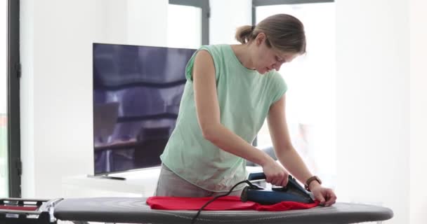 Μια κουρασμένη γυναίκα στο σπίτι χαϊδεύει μια μπλούζα με σίδερο, ένα κοντινό πλάνο. Εργασία, σιδέρωμα, αργή κίνηση - Πλάνα, βίντεο