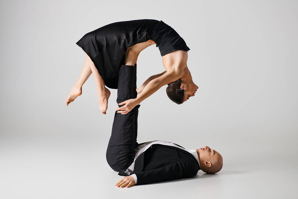 flexible young woman in black attire balancing on bare feet of her dancing partner on grey backdrop - Фото, изображение