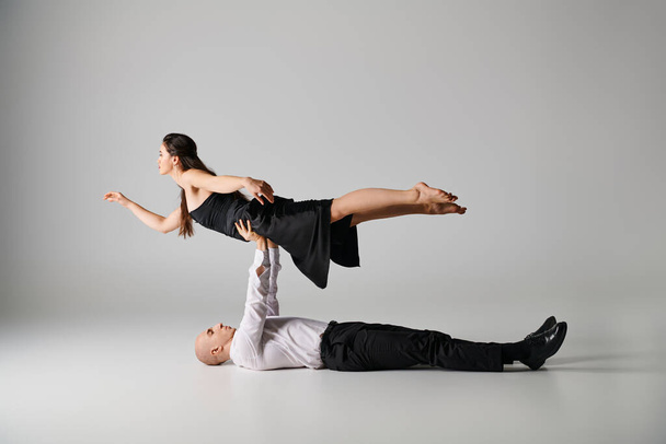 hombre acostado en el suelo y levantando el cuerpo de la mujer en vestido durante la actuación de baile sobre fondo gris - Foto, Imagen