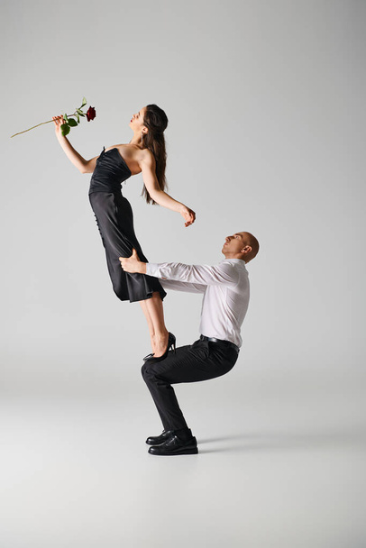 young woman in dress with red rose balancing on laps of dancer in formal attire during performance - Photo, Image