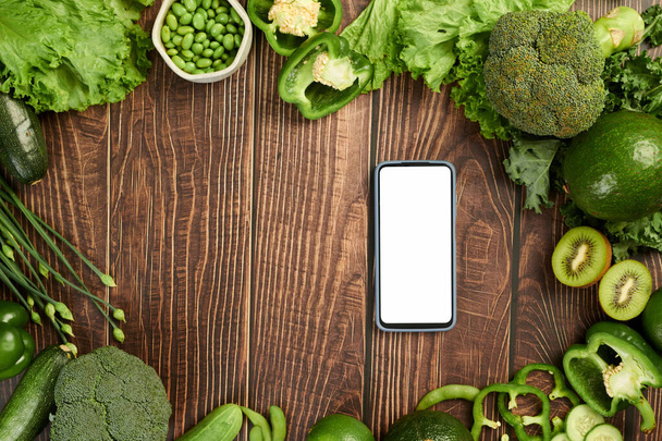 Grünes Gemüse und Obst auf Tisch und Smartphone mit leerem Bildschirm - Foto, Bild