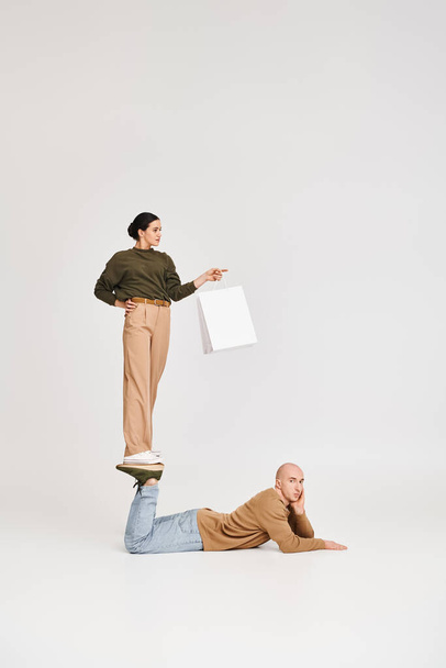 fiatal nő alkalmi viselet bevásárló táska kiegyensúlyozó lábán férfi játékos pózban a stúdióban - Fotó, kép