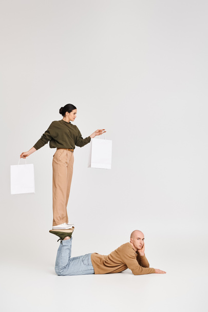 mujer joven en traje casual con bolsas de compras equilibrio en las piernas del hombre en una pose lúdica en el estudio - Foto, imagen