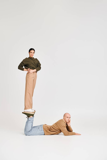 молодая женщина в повседневной одежде балансирует на ногах мужчины в игривой позе в студии на сером фоне - Фото, изображение