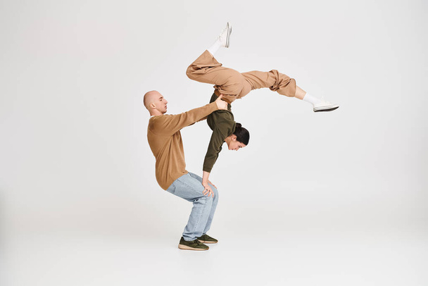 Pár alkalmi öltözékben végző bonyolult akrobatikus egyensúly stúdió szürke háttér - Fotó, kép