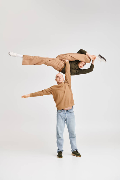Paar in lässiger Kleidung führt dynamische akrobatische Balance im Studio auf grauem Hintergrund vor - Foto, Bild