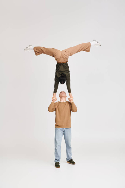 duo acrobat artístico com mulher na cabeça apoiada por homem ajoelhado em estúdio em fundo cinza - Foto, Imagem