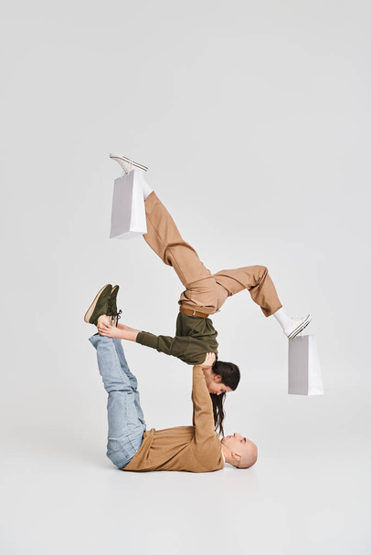 Akrobatisches Paar, junge Frau mit Einkaufstüten auf Beinen balanciert mit Unterstützung des Mannes im Studio - Foto, Bild