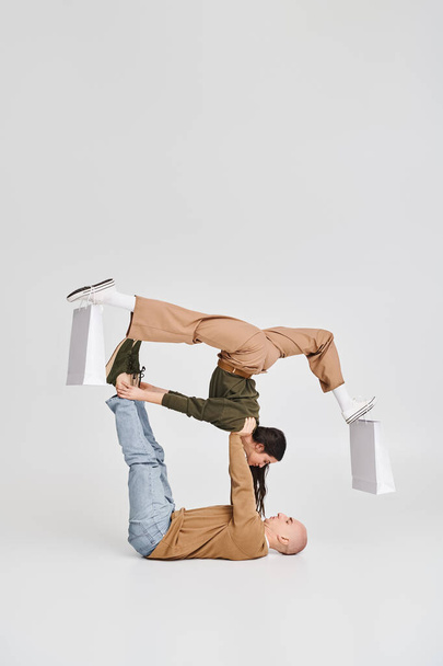 Akrobatikus pár, nő bevásárló táskák a lábon kiegyensúlyozó férfi támogatásával a stúdióban - Fotó, kép