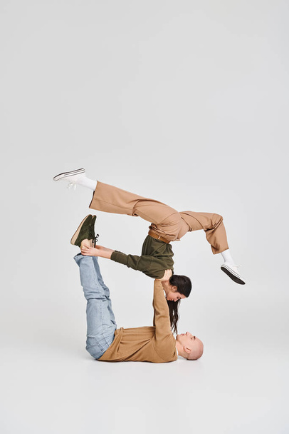 Akrobatisches Paar, junge brünette Frau in lässiger Kleidung balanciert mit Unterstützung eines Mannes im Studio - Foto, Bild