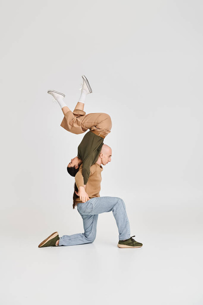 брюнетка женщина балансирует вверх ногами с поддержкой мужчины в повседневной одежде во время репетиции в студии - Фото, изображение