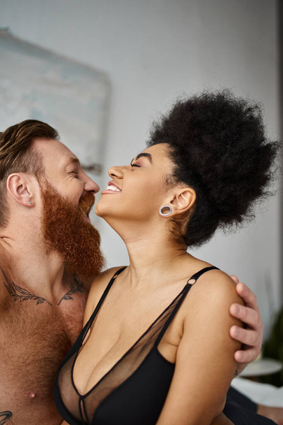 ευτυχισμένος άντρας με τατουάζ που αγκαλιάζει την Αφροαμερικανή φιλενάδα του στο σουτιέν, πολυπολιτισμικό σέξι ζευγάρι - Φωτογραφία, εικόνα