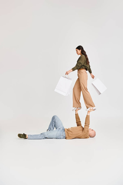 женщина в повседневной одежде держа сумки и балансируя на руках мужчины, пара акробатов - Фото, изображение