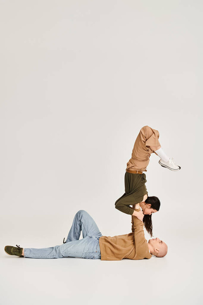 femme brune en tenue décontractée équilibrant sur les mains d'un homme fort, couple d'acrobates en studio - Photo, image