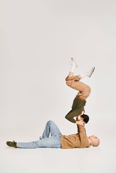 brunette jeune femme en tenue décontractée équilibrage sur les mains de l'homme fort, couple d'acrobates en studio - Photo, image