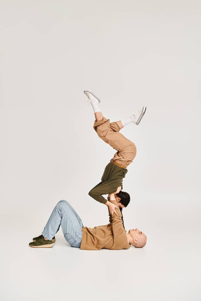 jeune acrobate féminine en tenue décontractée équilibrant sur les mains d'un homme fort, répétition en couple en studio - Photo, image