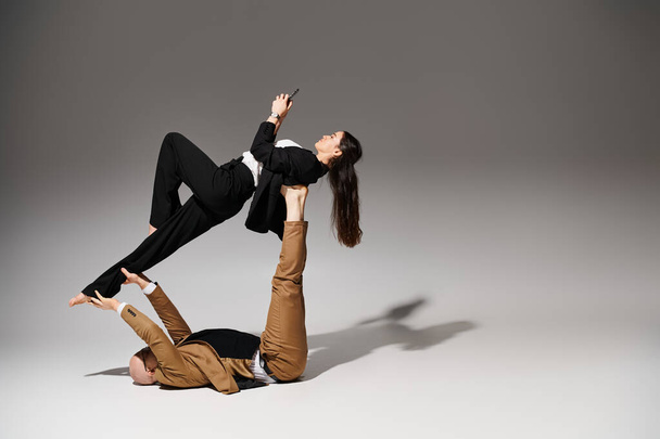 Nainen liike-elämän vaatteet älypuhelin tasapainotus jaloissa ja käsissä mies, pari akrobaatteja - Valokuva, kuva