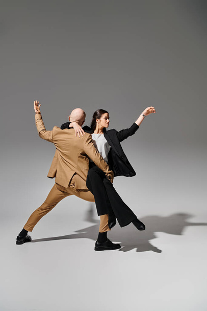 Business couple in suits perform a dynamic dance move in the studio with grey background, acrobats - Photo, Image