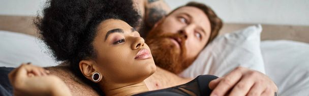 giovane e riccia donna afroamericana in lingerie sdraiata accanto al suo uomo in camera da letto, striscione - Foto, immagini