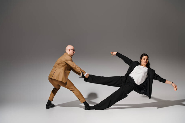 Dynamic dancers in business attire performing a balancing act in a studio with grey background - Photo, Image