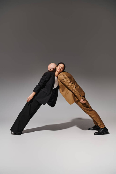 Joven pareja artística en traje de negocios realizando un movimiento de baile espejo en estudio con fondo gris - Foto, Imagen