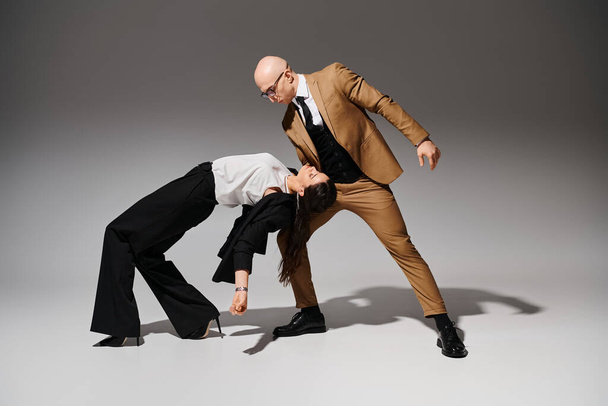 Üzleti partnerek egy összehangolt táncmozdulatban, összeöltözve a stúdióban szürke háttérrel - Fotó, kép