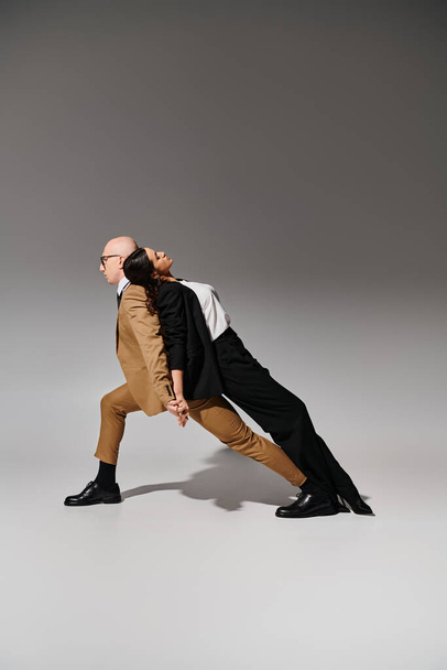 Tanzpartner bewegen sich, Frau im Anzug lehnt sich auf den Rücken des Mannes in Businesskleidung vor grauem Hintergrund - Foto, Bild